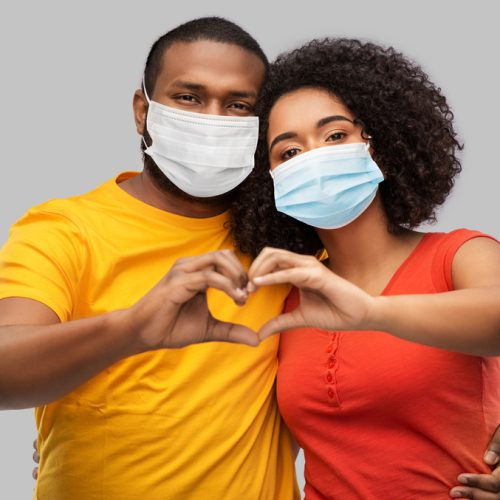 health, quarantine and pandemic concept - happy african american couple wearing protective medical masks for protection from virus making hand heart gesture over grey background